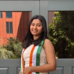 Young woman smiling in front of University Club entrance wearing tricolor sash.