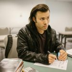 Focused student sitting at a desk during an exam in a classroom setting, writing on paper.